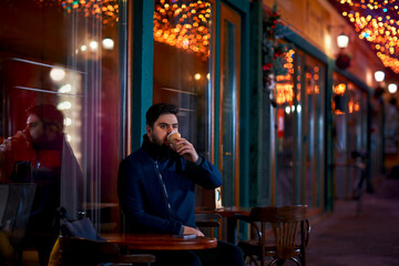 young adult man sitting alone in urban outdoor cafe on the night cozy narrow street