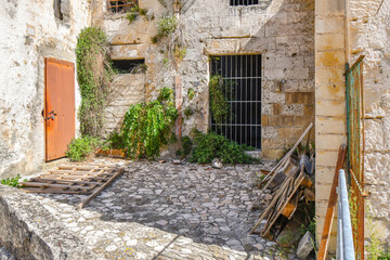 Fototapeta na wymiar A stray tabby cat sits outside the gate of an abandoned cave dwelling in a small courtyard in the ancient village of Matera, Italy, an Unesco World Heritage Site