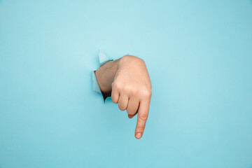Finger pointing down through torn blue paper wall. Hand gestures of direction.