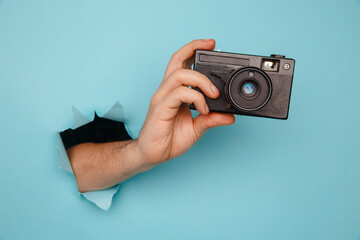 Hand holding camera from blue torn paper.