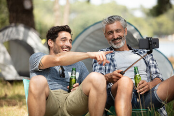 Fototapeta na wymiar two men friends drinking beer taking selfie in camping site