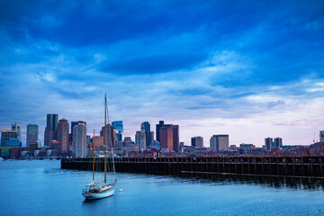 Evening photo of downtown panorama over Boston Main Channel with small sail boat yacht on forefront