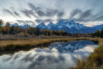 autumn evening shot of the snow covered teton mountains reflected in calm water at schwabachers...