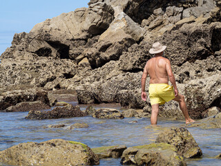 Hombre con bañador amarillo y sombrero mirando las rocas con textura en la Playa del Rosal en Cantabria, verano de 2020
