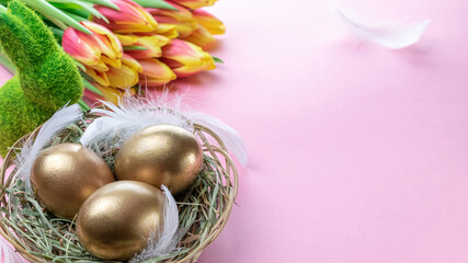 Egg color. Happy Easter decoration: golden colour eggs in basket with spring tulips, white feathers on pastel pink background. Foil minimalist egg design, modern template.