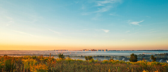 View of the city of Oryol in the morning at dawn in the fog, flowering field herbs in the foreground
