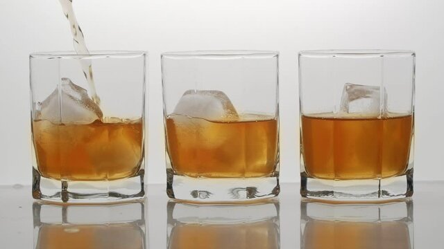 Slow Motion Shot of Pouring Ice Tea or whisky into Glass with Ice, Isolated on White Background.