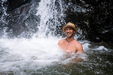 Latin man bathing in the waterfall with a hat