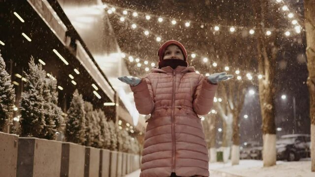 Portrait of a young enthusiastic girl on the Christmas decorated street during a snowfall