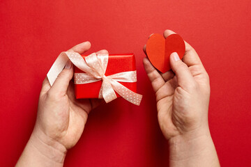 Gift box with ribbon in female hands on red background