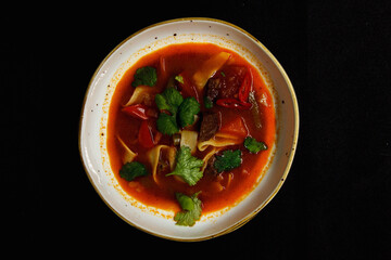 Spicy soup in a deep plate on a black background