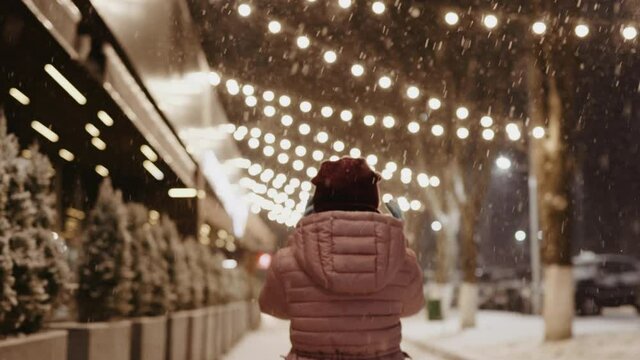 young girl on the street decorated for Christmas during a snowfall,rear view