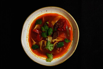 Spicy soup in a deep plate on a black background