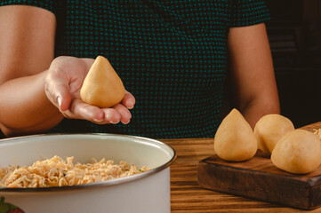 Hands of woman preparing brazilian croquette (coxinha de frango) on a wooden kitchen table