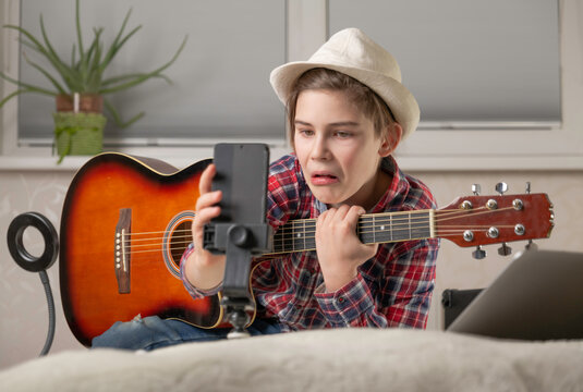 Boy learning or takes off the vlog to play guitar through a video call, home music lessons, hobby, vlogging and creation concept. Young guitarist guy videobloger play the guitar in living room