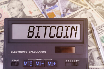 On the table are dollars and a calculator on the electronic board which says BITCOIN