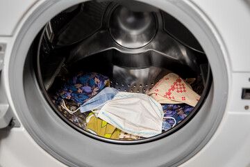 Lot of homemade textile reusable protective face masks inside washing machine, ready to wash. Home indoors.