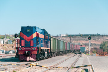 Locomotive with container train on railroad tracks at industrial cargo shipment area. Number on front of loco contains cyrillic letters and numbers 'TEM2U 8517'