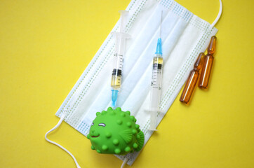 The concept of treatment and vaccination against coronavirus and other diseases. A toy representing the coronavirus, medical face masks, syringes and ampoules on a yellow background. Flatley.