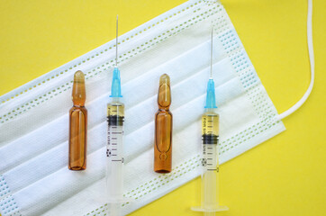 The concept of treatment and vaccination against coronavirus and other diseases. Medical face masks, syringes and ampoules on a yellow background. Flatley.