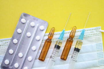 The concept of treatment of coronavirus and other diseases. Medical face masks, pills, syringes, and ampoules for the treatment of covid-19 on a yellow background. Flatley.