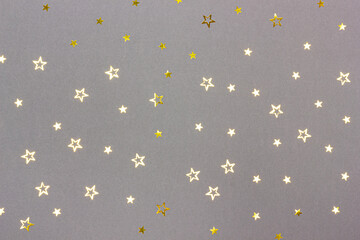 Festive gray background with scattered star shaped golden confetti. Top view. Flat lay style. Color trend 2021.