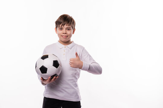 A happy young boy holding a soccer ball is showing a thumb up at the camera
