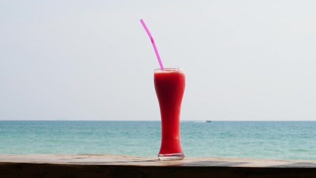Tall glass with fresh and cool watermelon juice on wooden counter at beach bar, blurred sea seen on background. Popular alcohol free drink served in Thailand cafe. Hand held shot