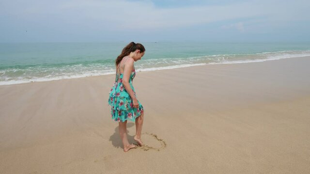 Woman draw heart shape on sand, using leg, then go away. Sea wave splash, water run up and wash out fragile picture. Tourist lady recreate at exotic island of Thailand