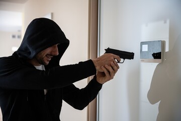 The hooded thief with a gun breaks into the apartment. Security alarm on the wall.