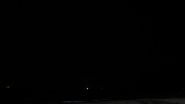 Dark cloudy sky over sea, bright flashes of thunderstorm lightning and illuminate heavy clouds around. Time lapse shot. Small lights of fishing boats seen on waver