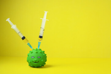 The concept of vaccination or coronavirus is depicted using a rubber toy fish with two syringes stuck in the body on a yellow background with a copy space