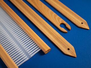 Wooden weaving tools jn the blue background: reed, shuttle and pickup sticks
