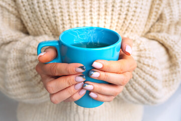 Woman in cozy woolen sweater warming cold hands with cup of hot tea or coffee.