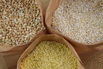 Buckwheat, pearl barley and millet, healthy groats in paper bags on jute fabric background