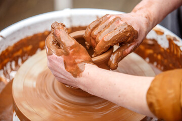 A potter makes dishes out of brown clay. Dirty worker's hands close up.