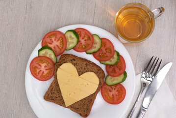 Heart shaped cheese sandwich with vegetables on white plate. Valentine's day breakfast