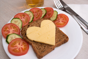 Heart shaped cheese sandwich with vegetables on white plate. Valentine's day breakfast