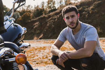 Young biker crouching next to his motorcycle looking at camera