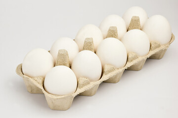 Ten white chicken eggs lie in two rows in a cardboard tray. The tray lies obliquely