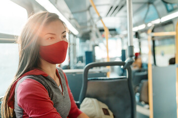 Woman wearing face mask inside public transport bus commuting to work. Asian girl passenger sitting with red facial fabric covering. © Maridav