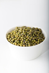 Bowl of uncooked mung beans on white background.