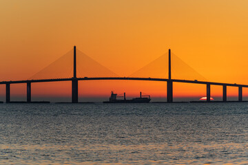 Fototapeta na wymiar Freighter sailing under bridge at sunrise