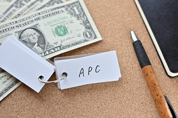 On the desk there are bills, a notebook, and a sticky note with the word APC written on it. It was an abbreviation for the financial term average propensity to consume.