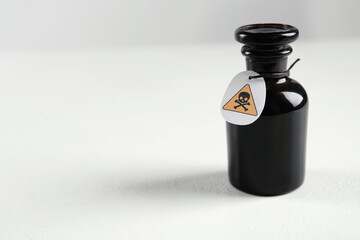 Glass bottle of poison with warning sign on light background. Space for text