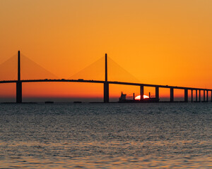 Fototapeta na wymiar Sunrise behind freighter while sailing under bridge