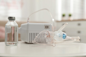 Modern nebulizer with face mask and liquid medicine on white table indoors. Inhalation equipment