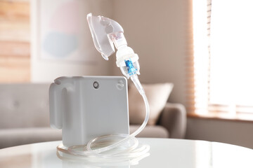 Modern nebulizer with face mask on white table indoors. Inhalation equipment