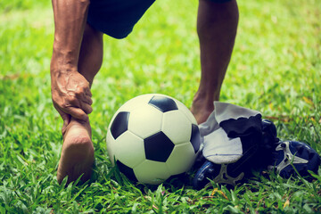 Soccer ball and sport shoes on green grass with soccer player catch the ankle of the feet because...