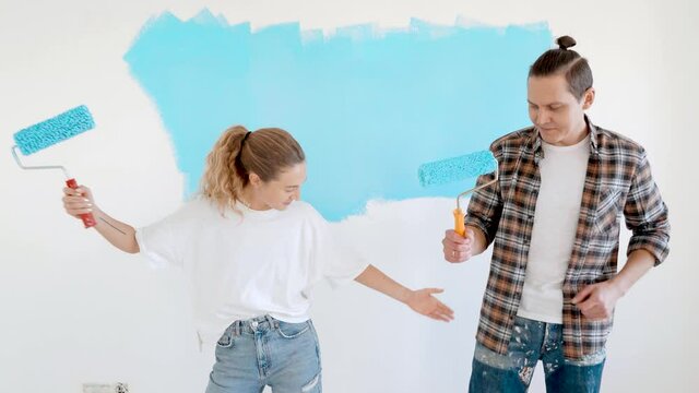 Married couple having fun while doing repair in their house. Wife teaches husband to dance with paint brush